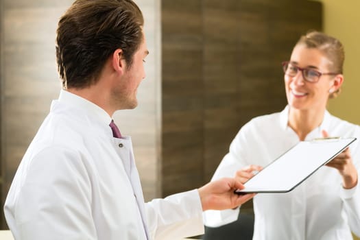 A doctor or dentist hands over a clipboard to his receptionist at the reception of his practice