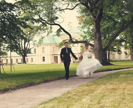 Groom and the bride run on a path in palace park