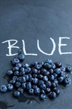 Fresh blueberries and word blue written in chalk on dark background