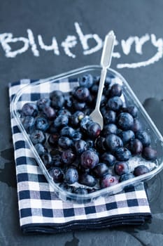Fresh blueberries and fork on checkered teatowel and word blueberry written in chalk on dark background