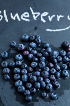 Closeup of fresh blueberries and word blueberry written in chalk on dark background