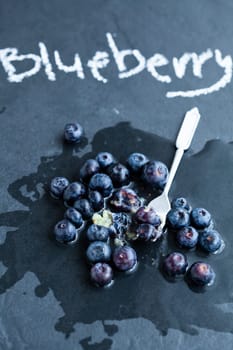 Fresh blueberries and fork and word blueberry written in chalk on dark background