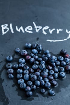Fresh blueberries and word blueberry written in chalk on dark background