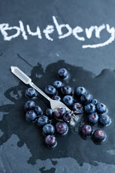 Fresh blueberries and fork and word blueberry written in chalk on dark background