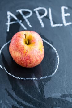 Juicy apple in circle and word apple written in chalk on dark background