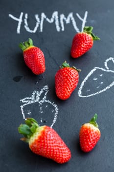 Fresh whole strawberries and chalk drawings and yummy word on dark background