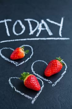 Three fresh whole strawberries inside chalk heart drawings and today word on dark background