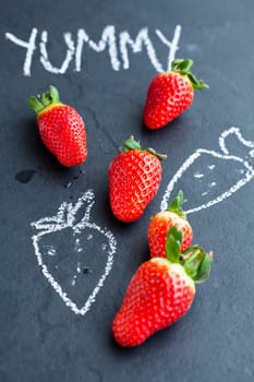 Fresh whole strawberries and chalk drawings and yummy word on dark background