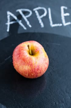 Juicy apple and word apple written in chalk on wet dark background