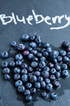 Closeup of fresh blueberries and word blueberry written in chalk on dark background