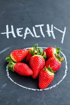 Fresh whole strawberries inside chalk circle and healthy word on dark background