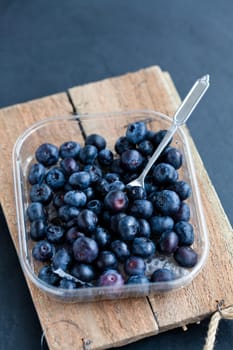 Closeup of fresh blueberries and fork on wooden serving tray on dark background