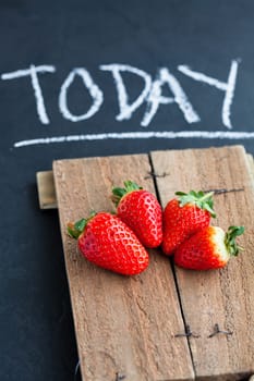 Three fresh whole strawberries on wooden serving tray with text written in chalk