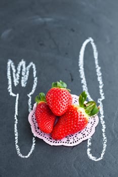Three fresh whole strawberries and chalk drawings of knife and fork on dark background