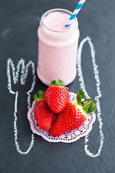 Three fresh whole strawberries and smoothie and chalk drawings of knife and fork on dark background