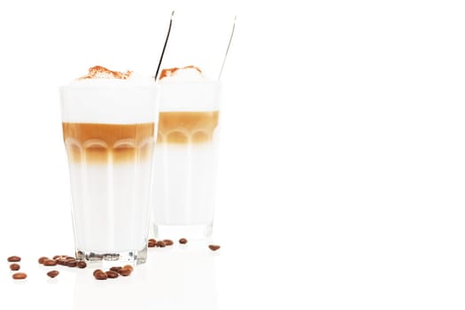 Latte macchiato in front of another latte Macchiato with coffee,beans and chocolate powder on white background