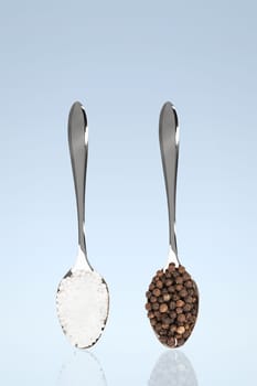 Salt and pepper on spoons against blue background