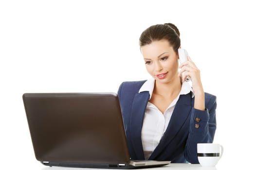 Smiling young business woman speaking on phone while using laptop, isolated on white