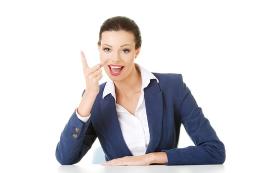 Business woman sitting at the desk and pointing with finger to empty copy space, isolated over white background