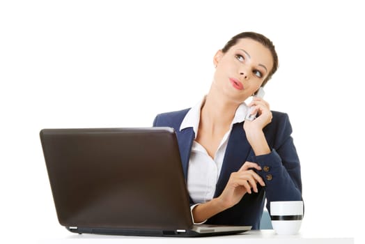 Smiling young business woman speaking on phone while using laptop, isolated on white