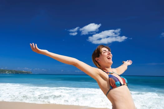 Beautiful young woman with arms open in a tropical beach enjoying the summer
