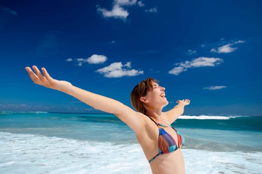 Beautiful young woman with arms open in a tropical beach enjoying the summer