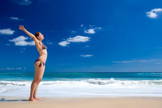 Beautiful young woman with arms open in a tropical beach enjoying the summer
