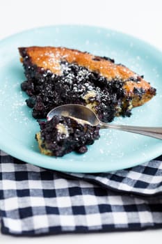 Closeup of slice of delicious blueberry pie on plate with spoon resting on checkered napkin over light background