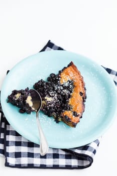 Closeup of slice of delicious blueberry pie on plate with spoon resting on checkered napkin over light background