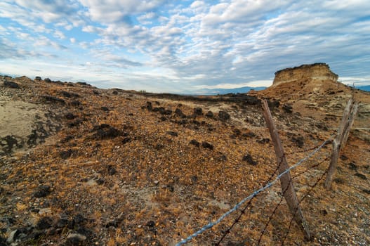 Fence extending in a rocky barren desert under a dramatic sky