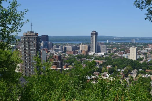 The view of downtown Hamilton with some high rises and a park in the foreground, and the lake Ontario in the background, from the mountain.
