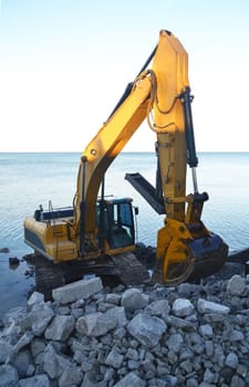 A heavy excavator fixing the shore line for erosion on lake Ontario, standing in the lake.