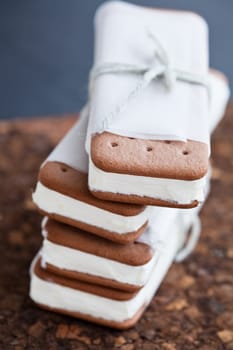 Closeup of stack of vanilla ice cream biscuits wrapped in white paper with string and bow resting on brown place mat