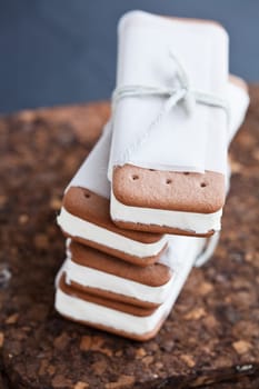 Closeup of stack of vanilla ice cream biscuits wrapped in white paper with string and bow resting on brown place mat