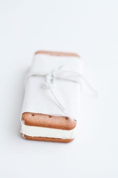 Closeup of vanilla ice cream biscuit wrapped in white paper with string and bow on light background
