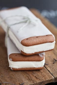 Closeup of two ice cream biscuits wrapped in white paper with string and bow resting on wooden serving surface