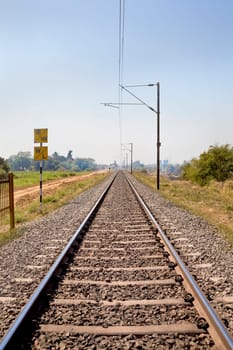Vertical landscape of railroad tracks in Indian cutting acrosss the rural countryside along the outskirts of o Gujarat village towards the city of Surat. Typical scene with litter thrown around and locals walking close by