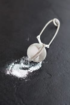 Closeup of sieve and icing sugar on dark textured background