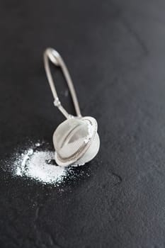 Closeup of sieve and icing sugar on dark textured background