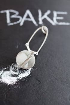 Closeup of sieve and icing sugar with word bake written in chalk on dark textured background