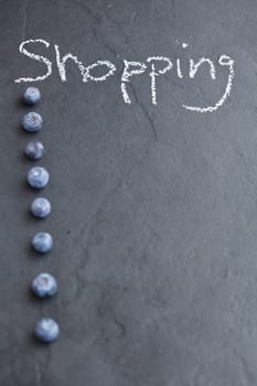 Closeup of shopping list background created from blueberries and word shopping written in chalk on dark background
