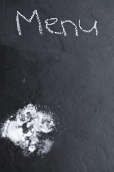 Closeup of dark background with icing sugar and word menu written in chalk