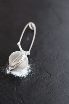 Closeup of sieve and icing sugar on dark textured background