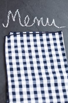 Closeup of checkered napkin and word menu written in chalk on dark background