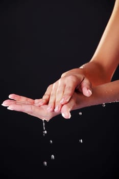 Water falling on female hands, over black background