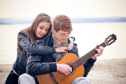 Young man with acoustic guitar and his girlfriend on the bach
