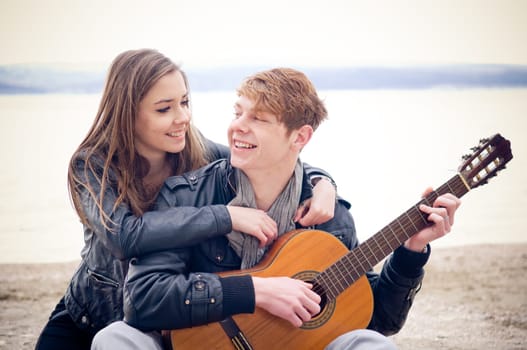 Young man with acoustic guitar and his girlfriend on the bach
