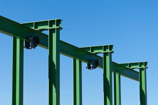 Detail of a small gantry crane painted green against the blue sky