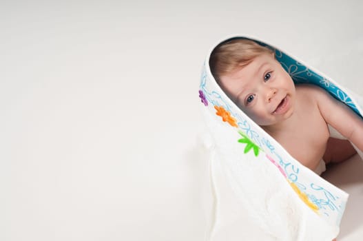 Happy little boy in white blanket with flowers in studio