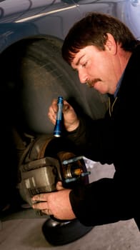 Uniformed Auto Technician Uses Mini Light to check brakes on a Car